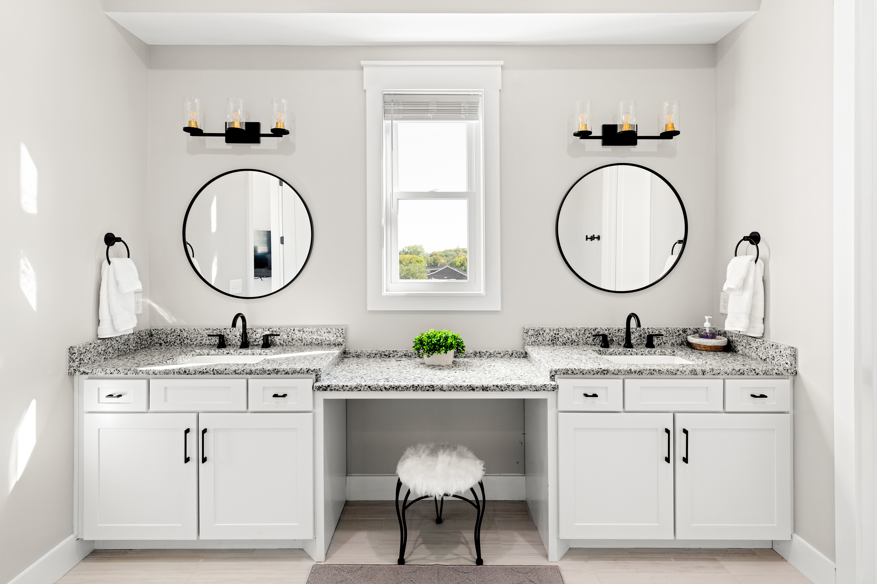 Bright bathroom with dual sinks, round mirrors, and vanity stool